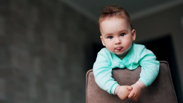 椅子の上に平和的に立っている周りを見渡す素敵な幼児 舌と笑顔を見せる愛らしい赤ちゃん ローアングルビュー — ストック動画