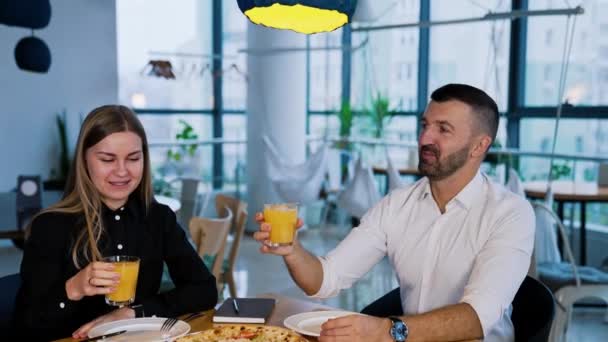 Ευτυχισμένοι Χαμογελαστοί Νέοι Άνθρωποι Χτυπάνε Ποτήρια Χυμό Καθισμένοι Στο Τραπέζι — Αρχείο Βίντεο