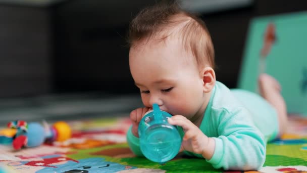 小さな赤ちゃんはボトルを扱うのに忙しい 素敵な髪型の素敵な子供は一人で水を飲もうとしています クローズアップ — ストック動画