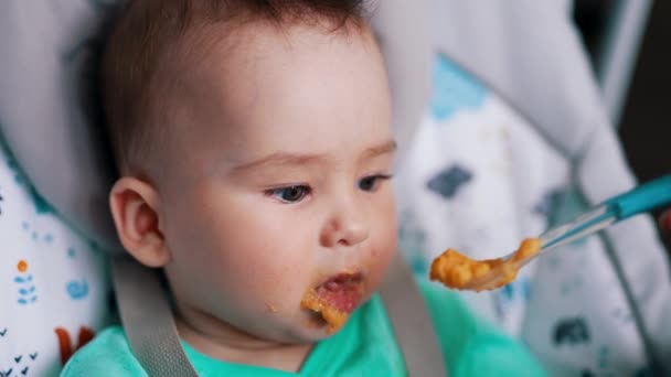 赤ちゃんの椅子に座っている小さな子供の栄養 美しい子供にはオレンジ色のスプーンが与えられます クローズアップ — ストック動画