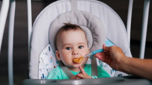 男婴的营养在就餐时间 给可爱的婴儿食物 他高兴地挥挥手 露出舌头 — 图库视频影像