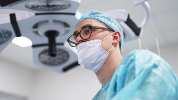 戴着口罩 帽子和眼镜的年轻男医生 医护专业人员的肖像以工作为重点 低角度视图 — 图库视频影像