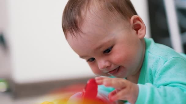 かわいい赤ん坊はおもちゃで遊ぶのに忙しい おもちゃに注意深く触れ 興味を持って舌を突き出している素敵な少年 サイドビュー — ストック動画