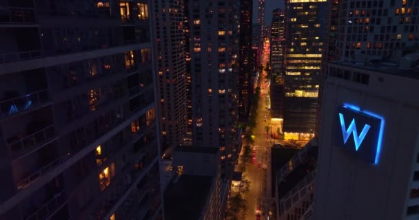 夜はシカゴのダウンタウンの明るい通り ドローン映像は 忙しい道路の上に素晴らしい超高層ビルの間に降下する — ストック動画