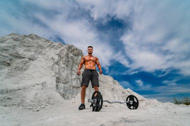 Beyaz kumların üzerinde halterle egzersiz yapan kaslı adam.