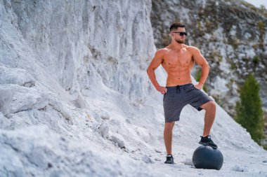 Kaslı adam plajda topla egzersiz yapıyor.