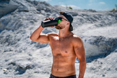 Kaslı üstsüz adam idmandan sonra su içiyor.
