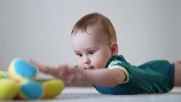 活泼的婴儿挥手躺在地板上 白人小孩想摸到他面前的玩具浅色背景模糊 — 图库视频影像