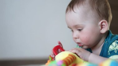 Tombul yanaklı en tatlı bebek parlak bir oyuncakla oynar. Sevimli çocuk oyuncaktan uzaklaşıyor ve yumruğunu ağzına sokuyor..
