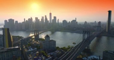 Manhattan ve Brooklyn Köprüleri, East River üzerinde, Golden Hour 'da. Turuncu gökyüzünün arka planında vurucu gökdelenlerin puslu siluetleri.