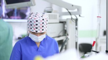 Kalp ve cerrahi maske takan şapkalı güzel bayan hemşire ameliyathanede çalışıyor. Sıhhiye tezgahı değiştiriyor.