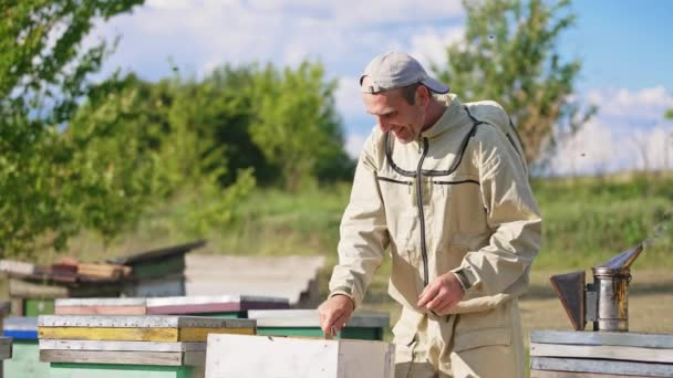 ハッピー笑顔の男性の養蜂家は ハイブからフレームを抽出するために金属製の器具を使用しています 男はフレームをピックアップし それをカメラに示す — ストック動画