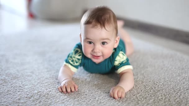 陽気で幸せなコーカサス人の赤ん坊の少年は 腹の笑顔に横たわっています 積極的に床の上に手足を叩く愛らしい子供 — ストック動画