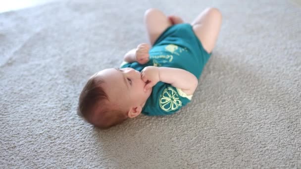 美しい幼児は 口に指を握っている床に横たわっています 小さな穏やかな赤ん坊は彼の頭の上にカメラを見る — ストック動画