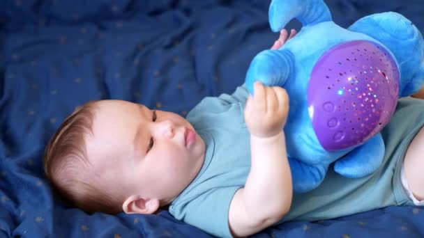 漂亮的白人男婴手里拿着柔软的玩具好孩子把注意力从看相机的玩具上转移开 然后又转向他的玩具 靠近点蓝色背景 — 图库视频影像