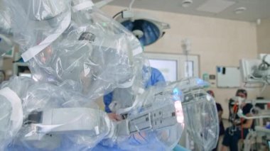 Modern ameliyathanede çalışan gelecekçi Da Vinci robotu. Arkaplanda operasyon sürecini izleyen doktorlar var. Bulanık arkaplan.