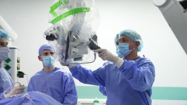 専門の外科医が顕微鏡を患者に前進させました 操作された患者の精密な技術装置を調節するスペシャリスト — ストック動画