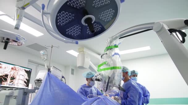 顕微鏡を見ている患者を操作する手術専門家 技術的に装備された手術室での低角度ビュー — ストック動画