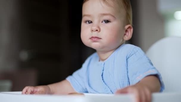 认真体贴的男婴坐在桌旁 小孩在玩食物 把百吉饼扔在地板上 看着它 靠近点 — 图库视频影像