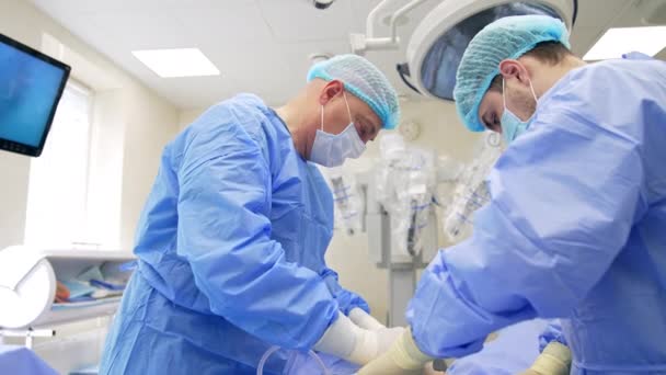 Nad Pacientem Skláněla Dvojice Lékařů Maskách Čepicích Modrých Pláštích Lékaři — Stock video