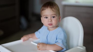 Güzel küçük çocuk sakince yemek masasında oturuyor. Tatlı çocuk elinde bir simit tutarak arkasını dönüyor..