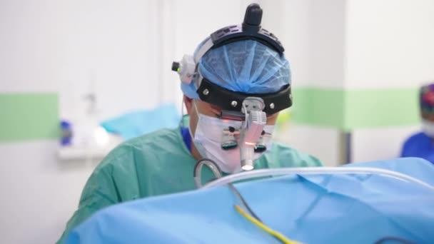 特殊な装置メガネを装備した外科医が手術を行います バックドロップの現代機器と医療スタッフ — ストック動画