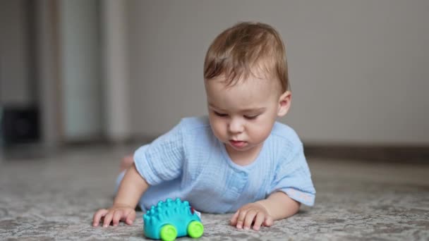 Uroczy Chłopiec Niebieskich Ciuchach Leży Brzuchu Podłodze Cute Dziecko Zabawkę — Wideo stockowe