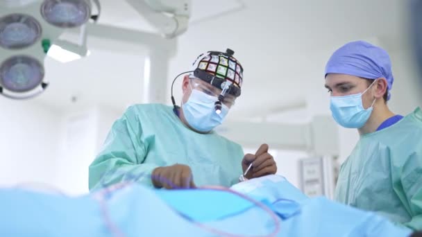 外科医のオトリガー科医が鼻腔手術を行っています デバイスメガネのプロフェッショナルは 手術を行うための機器を使用しています ブラーレッド バックドロップ — ストック動画