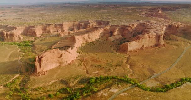 美国犹他州美丽峡谷的风景画 岩石上的无人机镜头穿过该地区的道路和沙漠中很少生长的绿色植物 — 图库视频影像