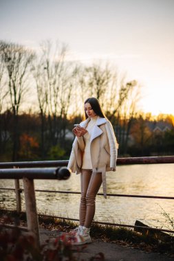 Genç bir kadın parkta yürürken akıllı telefonunu kullanıyor.