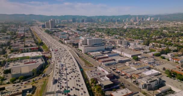 宽阔的多车道高速公路上满是行驶的汽车 飞越阳光灿烂的洛杉矶 加利福尼亚 背景下的朦胧小山 — 图库视频影像