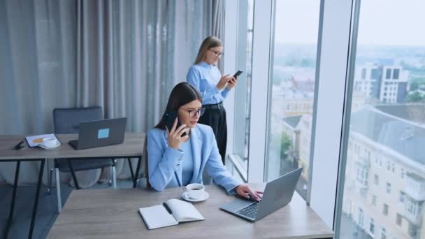 上班时间工作效率高的办公室员工 使用电话和笔记本电脑的女同事 背景为全景窗的办公室 — 图库视频影像