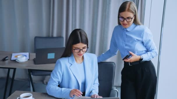オフィスで働く女性が仕事の問題について話し合う 女性の同僚はノートパソコンを見てメモを取る オフィスバックドロップ — ストック動画