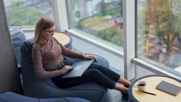 Büyük Pencerenin Yanında Oturan Düşünceli Genç Bayan Bilgisayarını Açar Çalışmaya — Stok video