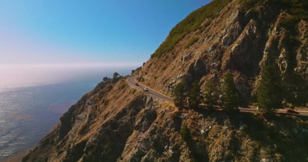 車が速く移動する山の高速道路 青い澄んだ空の背景にある海によるビッグサーモロ湾の美しい岩 — ストック動画