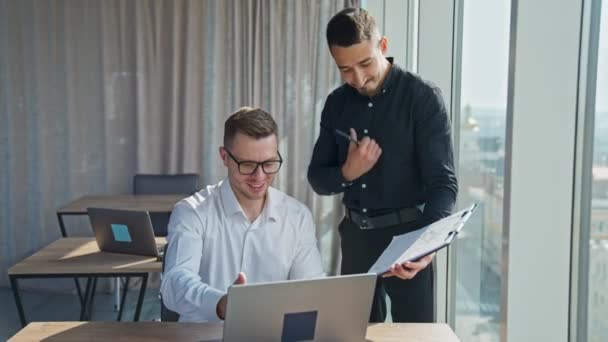 職場で協力するハッピーレジリエントオフィス従業員 紙を見ている男性 そしてコンピュータのラップトップ画面で — ストック動画
