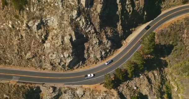 汽车在山中的双行道上疾驰而过 阳光普照的日子 高高的岩石覆盖着苔藓和罕见的灌木丛 — 图库视频影像