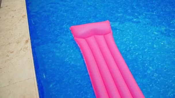 蓝色水中的长粉色充气床垫 床垫在游泳池的水边漂流 从顶部查看 — 图库视频影像