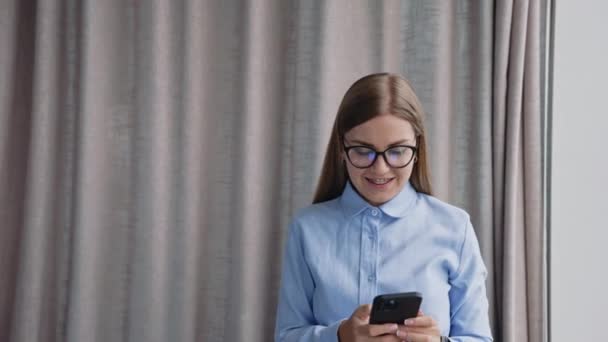 聪明的年轻女性戴着眼镜 蓝色衬衫 开始电话交谈来到窗前 坐在办公桌前的同事们 — 图库视频影像