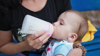 Şişeden süt emen tatlı bebek. Annesinin kucağına uzanmış güzel bir çocuk yemek yiyor. Kapat..