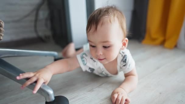 可爱的婴儿爬到地板上 触摸着椅子的轮子 相机快速接近可爱的男孩 他带着好奇触摸相机 靠近点 — 图库视频影像