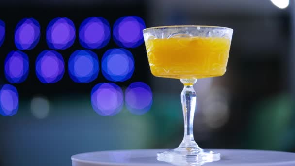 白色的旋转餐桌 配上一杯鸡尾酒 加满桔子饮料的大酒杯 靠近点蓝光背景模糊 — 图库视频影像