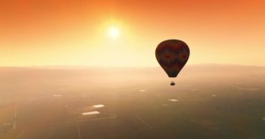 Turuncu gökyüzünde süzülen renkli sıcak hava balonu. Aerostat gün batımında vadinin üzerinde uçuyor. Üst görünüm.