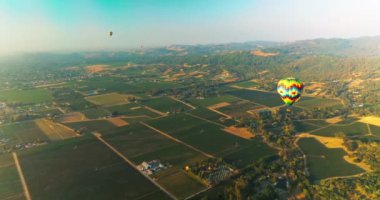 Açık mavi gökyüzünde süzülen parlak sıcak hava balonları. Havacılar Napa, Kaliforniya 'nın yeşil vadisinde uçuyorlar. Hava görünümü.