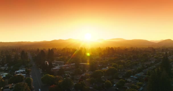 太陽を設定する明るい暖かい光の美しい居心地の良い緑の街 山の後ろに太陽が隠れている 背景にあるオレンジ色の空 エアリアルビュー — ストック動画