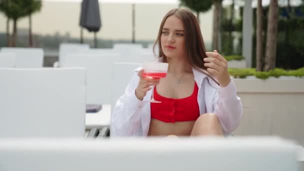 在炎炎夏日的游泳池边喝鸡尾酒 穿着红色泳衣的年轻貌美的黑头发姑娘喝着葡萄酒中的红葡萄酒 — 图库视频影像