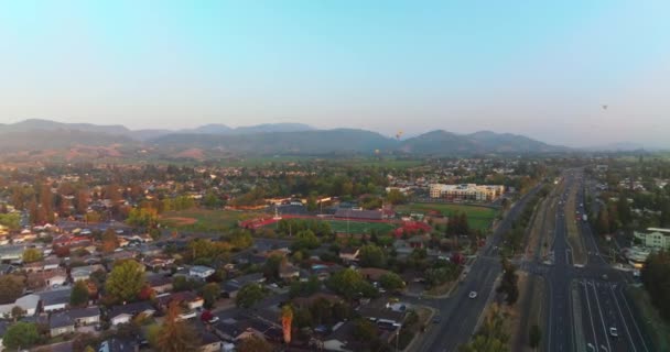 舒适的绿色城市的美丽全景 很宽的路 有交通工具经过 在高山蓝天的背景下飞行的热气球 — 图库视频影像