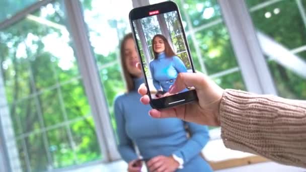 スマートフォンを持ち ビデオを撮る女性手 クローズアップ ダークヘアの魅力的な女性 ブルーのドレス 撮影のためのポーズ — ストック動画