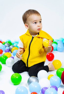 Küçük çocuk renkli toplarıyla top havuzunda oturuyor..