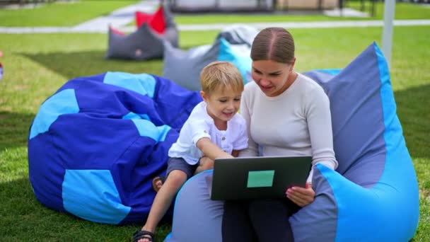 금발의 여자와 그녀의 아들은 노트북에 비디오를보고 의자에서 가족은 여름에 야외에서 — 비디오